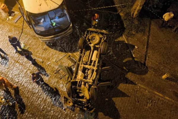 Acidente de carro em viaduto com veículo capotado e equipes de resgate no local.
