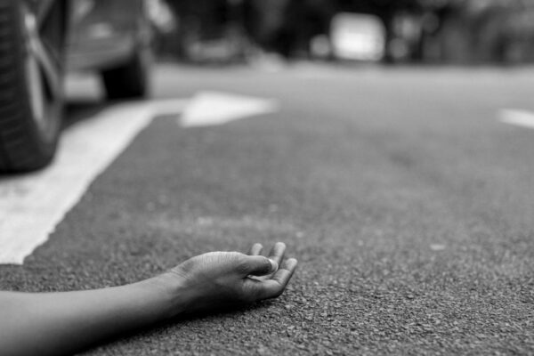 Acidente de trânsito em Nova Friburgo: corpo no asfalto com carro ao fundo.