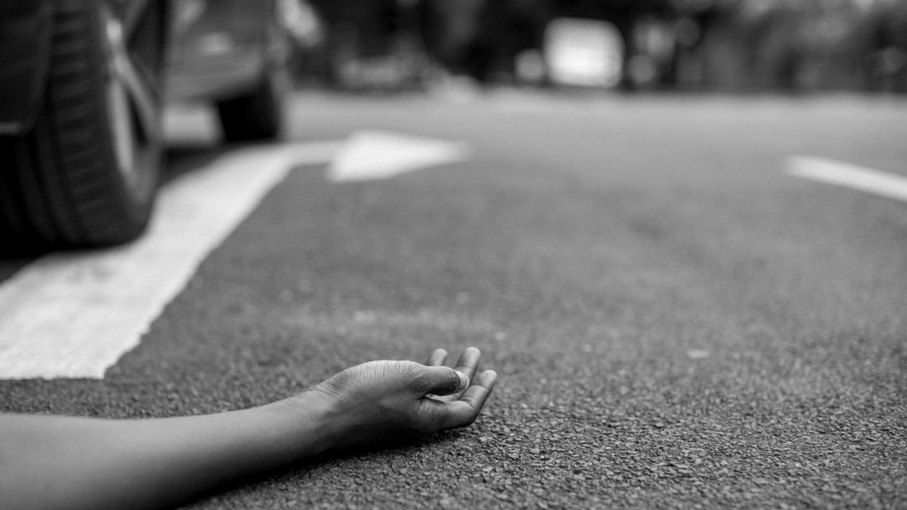 Acidente de trânsito em Nova Friburgo: corpo no asfalto com carro ao fundo.