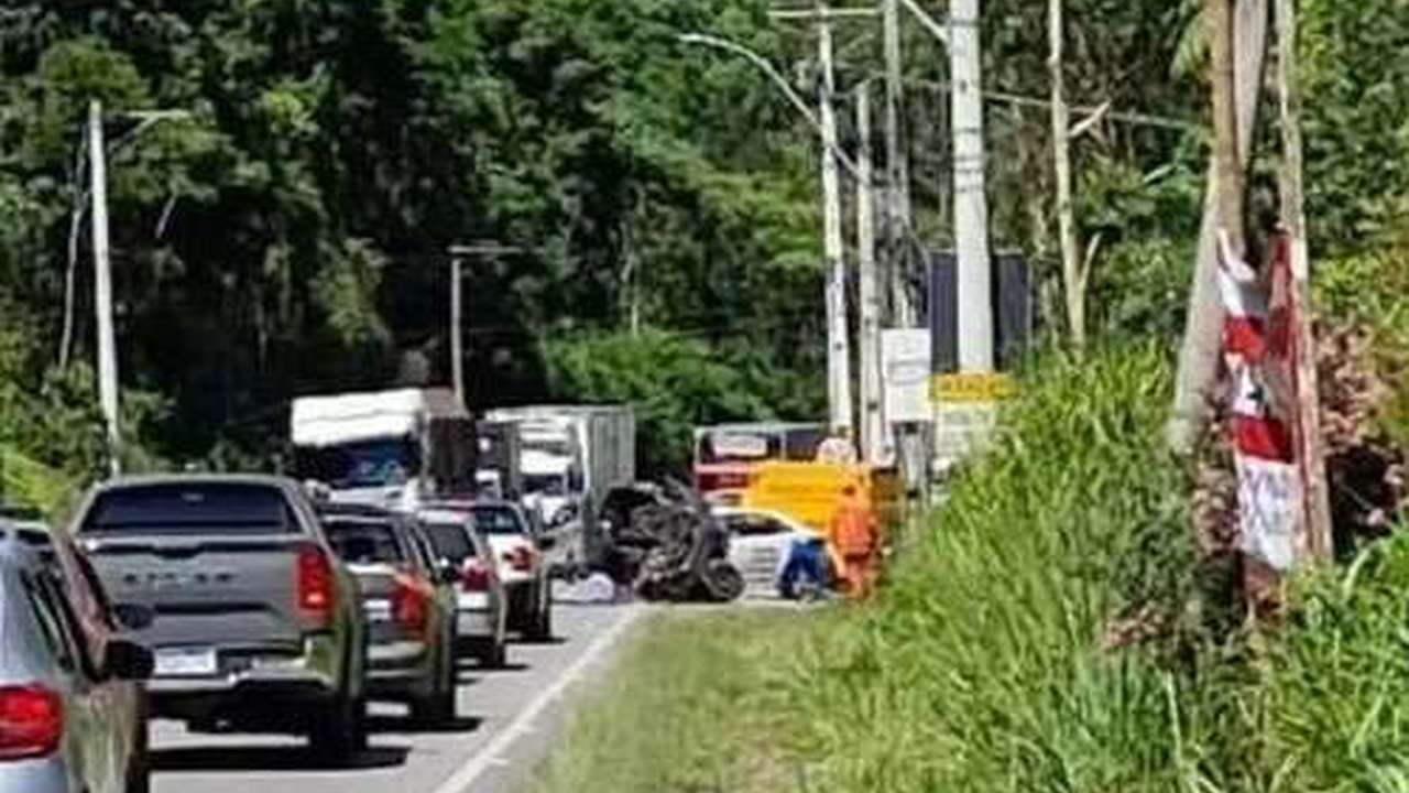 Acidente de trânsito na RJ-130 em Nova Friburgo: carro destruído e fila de veículos.