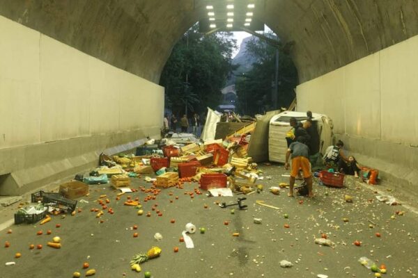 Acidente no Túnel Zuzu Angel: Caminhão tombado com carga de frutas espalhada.