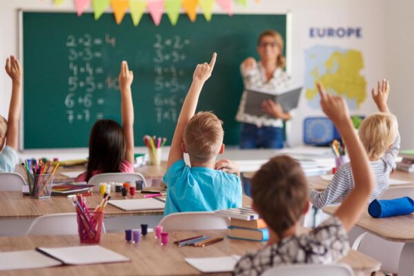 Alunos em sala de aula levantando a mão para responder, com foco na valorização docente.