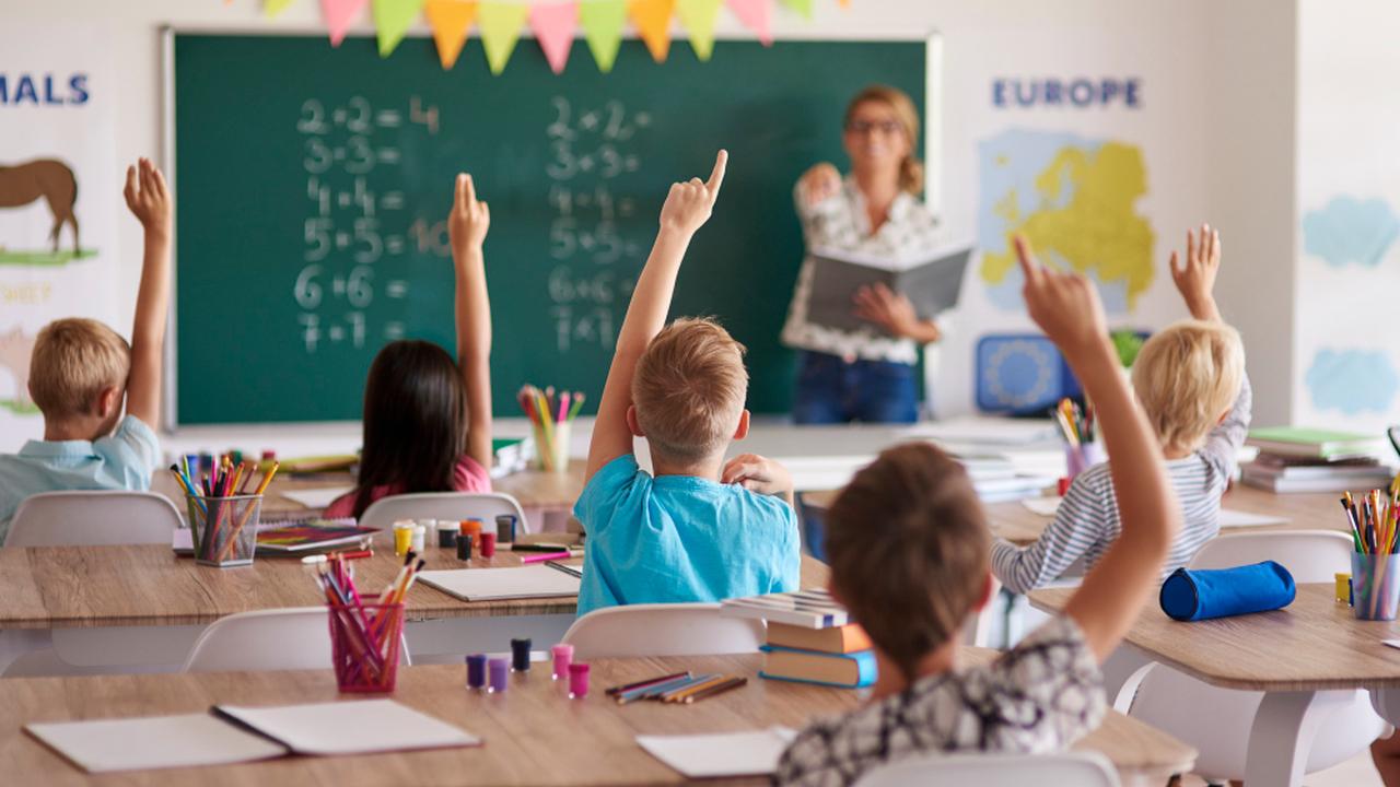 Alunos em sala de aula levantando a mão para responder, com foco na valorização docente.