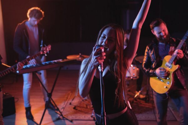 Banda de rock ao vivo com vocalista feminina cantando no palco, com outros músicos tocando instrumentos.