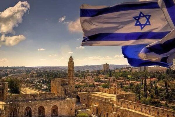 Bandeiras de Israel tremulando sobre uma cidade histórica, com edifícios antigos e um céu azul com nuvens.