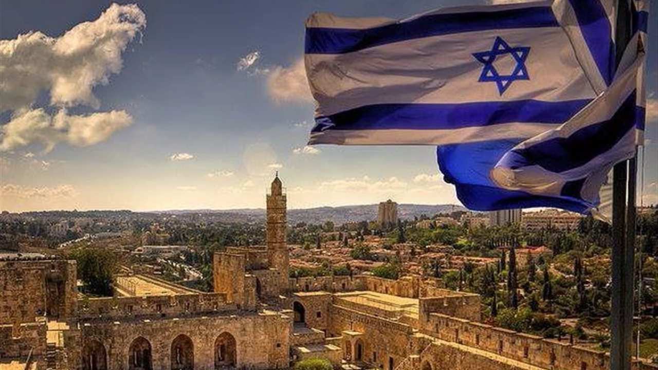 Bandeiras de Israel tremulando sobre uma cidade histórica, com edifícios antigos e um céu azul com nuvens.