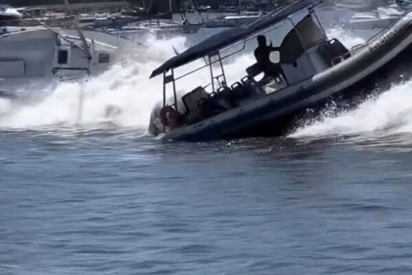 Barco em meio a ressaca na Baía de Guanabara, com ondas fortes e outro barco danificado ao fundo.