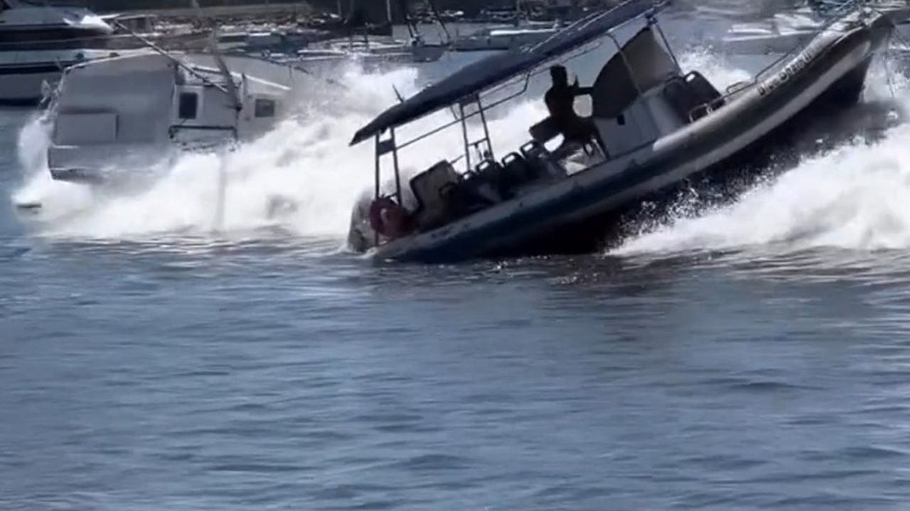 Barco em meio a ressaca na Baía de Guanabara, com ondas fortes e outro barco danificado ao fundo.