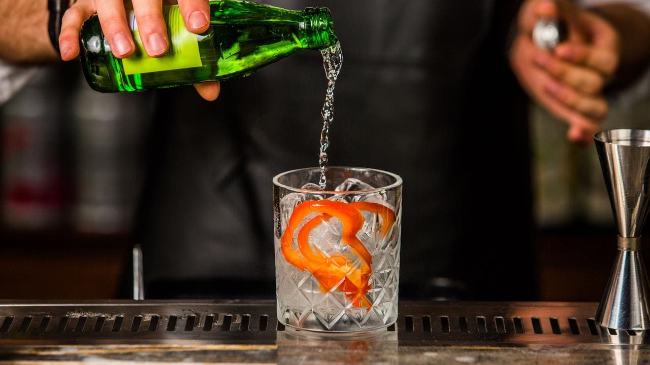 Barman preparando coquetel com gelo e frutas cítricas, possivelmente contendo álcool