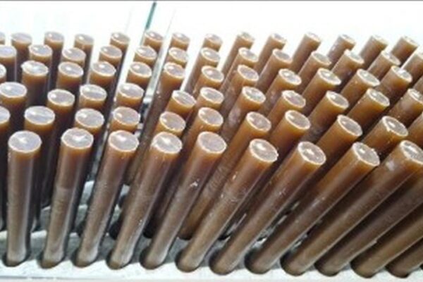 Bastões de cera marrom dispostos em fileiras, possivelmente em processo de fabricação.