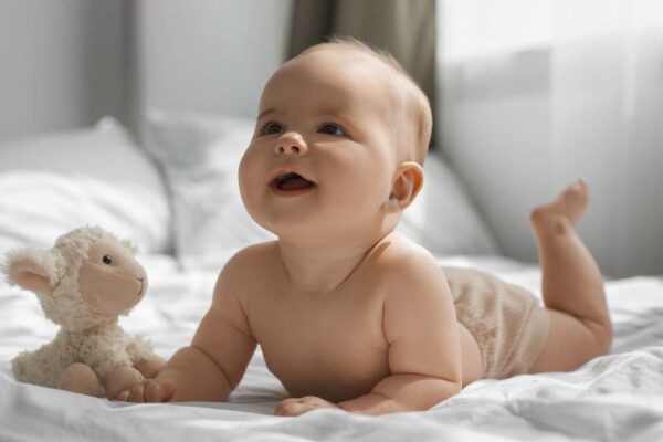 Bebê sorrindo com brinquedo de ovelha em cama.