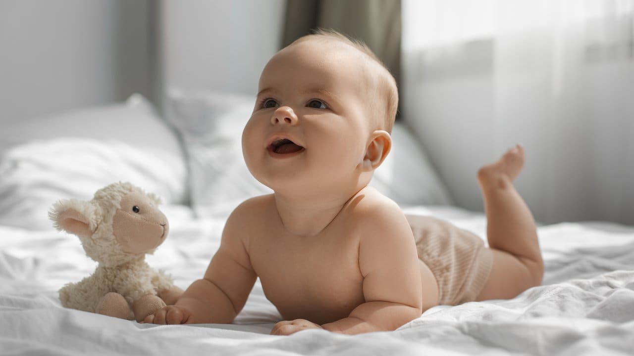 Bebê sorrindo com brinquedo de ovelha em cama.