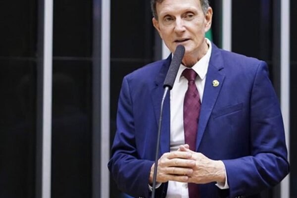 Bispo Marcelo Crivella falando em um evento, com um microfone na frente e um terno azul.