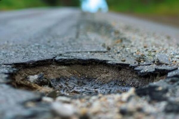 Buraco em estrada danificada, mostrando o asfalto rachado e deteriorado.