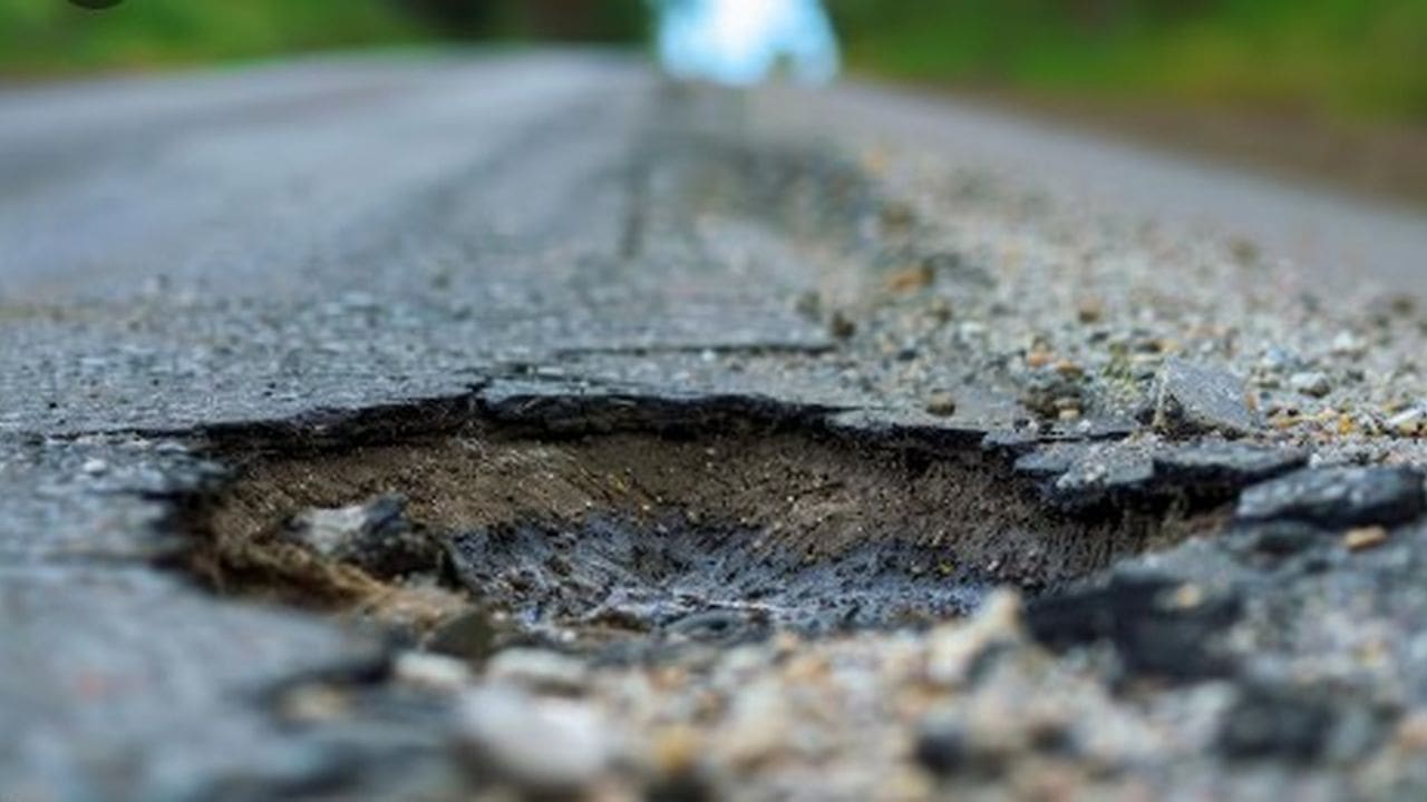 Buraco em estrada danificada, mostrando o asfalto rachado e deteriorado.