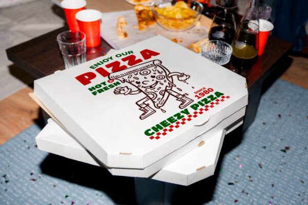 Caixa de pizza Cheezy Pizza em cima de mesa com copos e restos de comida.