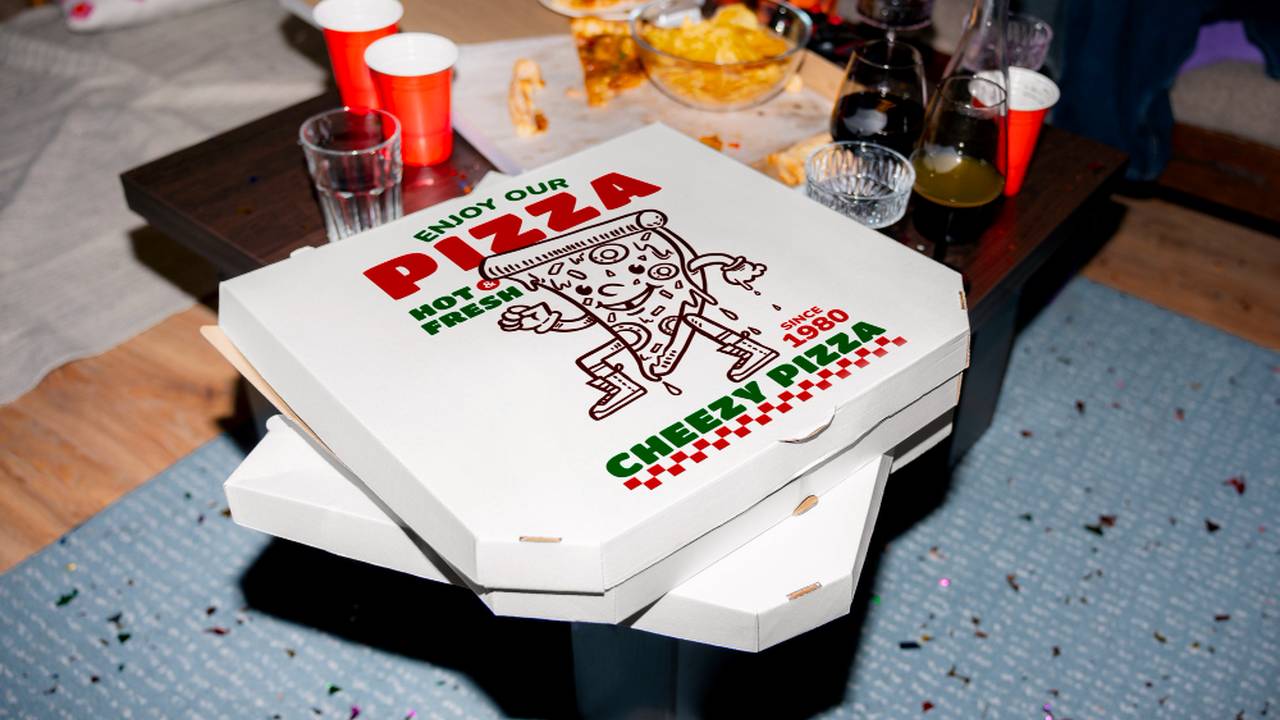 Caixa de pizza Cheezy Pizza em cima de mesa com copos e restos de comida.