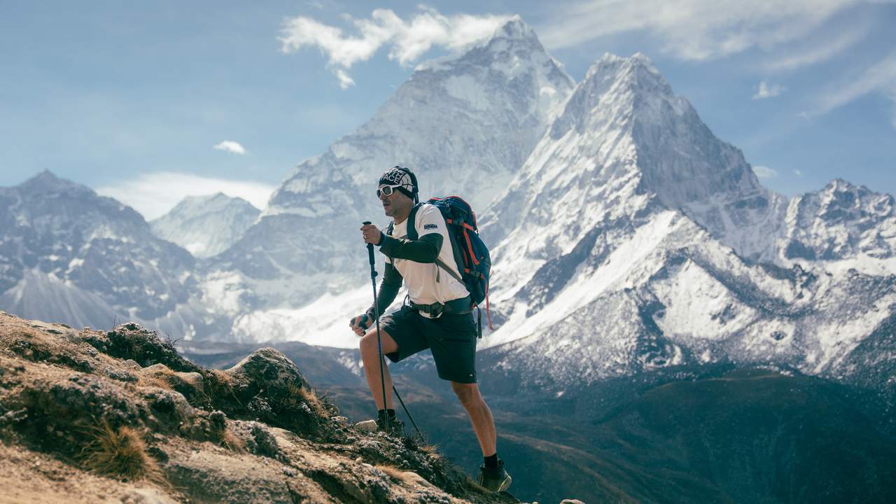 Caminhante escalando montanha nevada com bastões e mochila, em expedição ao Everest.