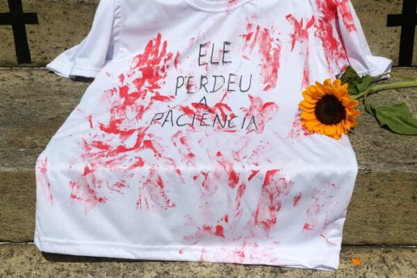 Camiseta branca manchada de vermelho com dizeres em protesto contra feminicídio.