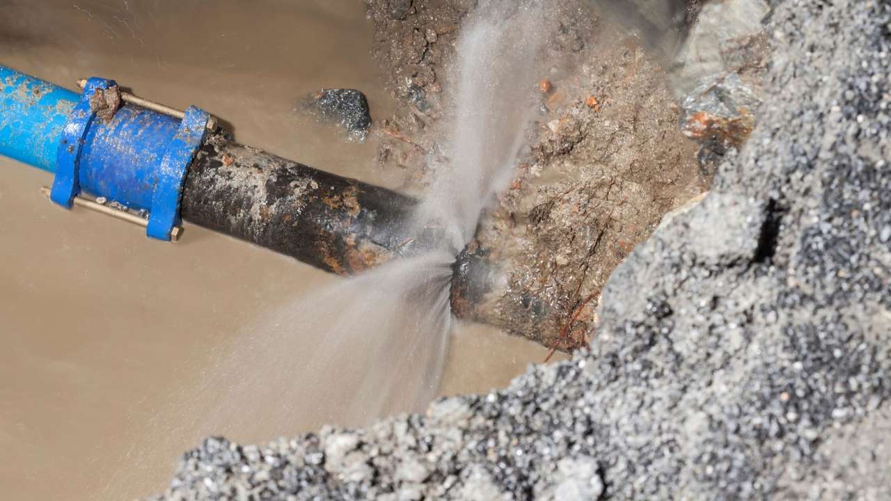 Canos de água danificados com vazamento em área alagada, mostrando a interrupção no abastecimento.