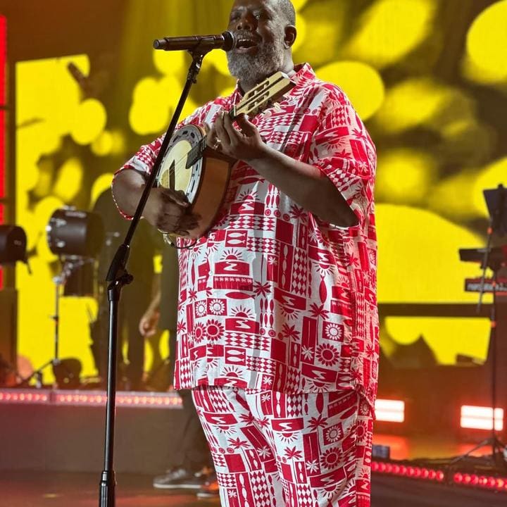 Cantor Péricles tocando violão e cantando no palco durante show musical.