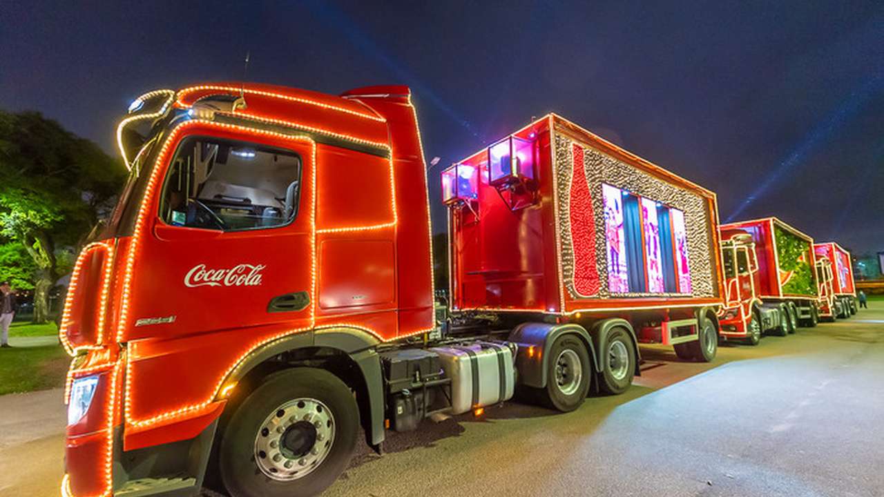 Caravana de Natal da Coca-Cola com caminhões decorados com luzes e telas exibindo imagens natalinas.