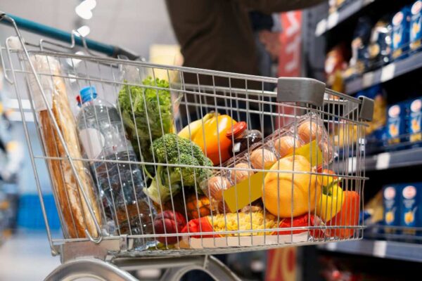 Carrinho de compras cheio de alimentos em supermercado, representando compras.