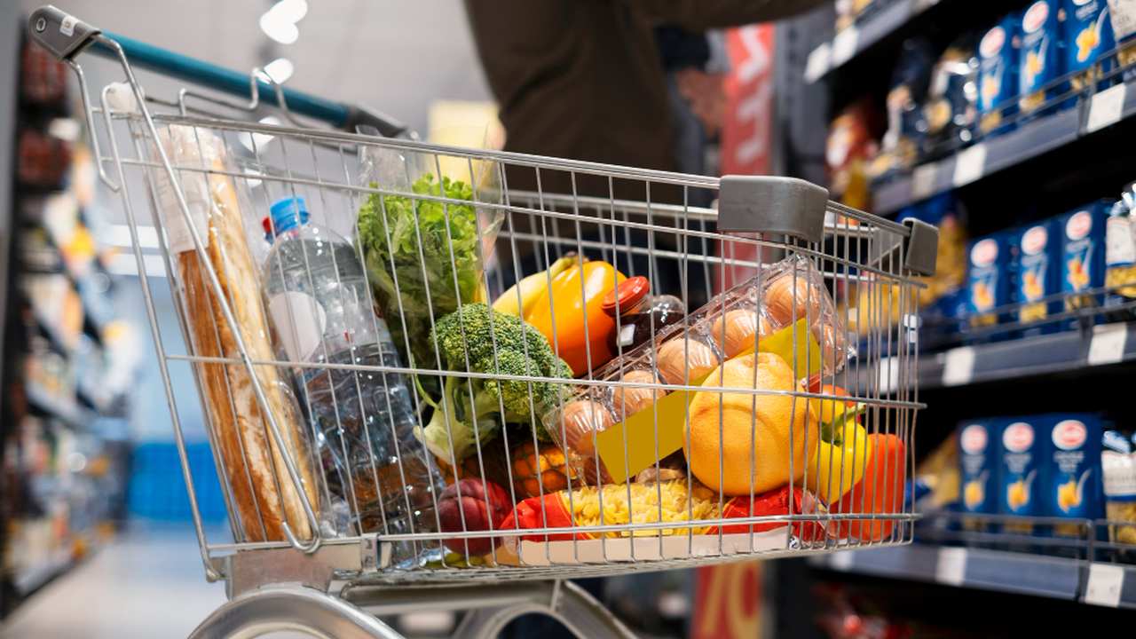 Carrinho de compras cheio de alimentos em supermercado, representando compras.