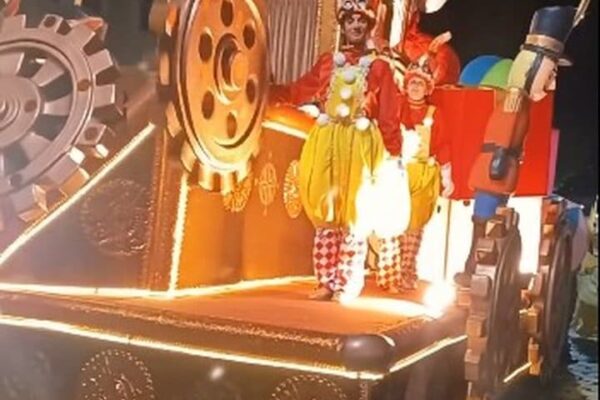 Carro alegórico de carnaval em destaque, com decoração elaborada e pessoas fantasiadas.