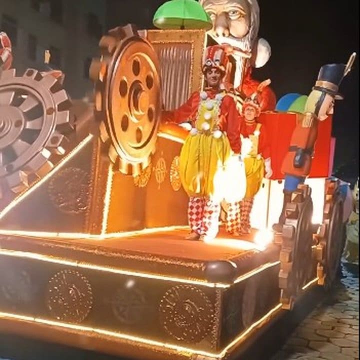 Carro alegórico de carnaval em destaque, com decoração elaborada e pessoas fantasiadas.