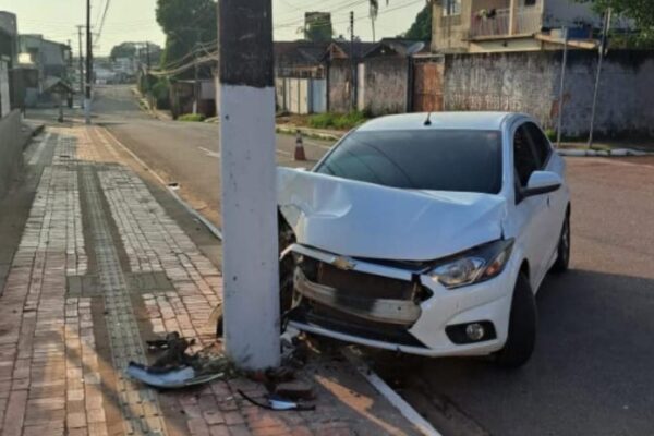 Carro branco danificado após colidir com poste em rua.