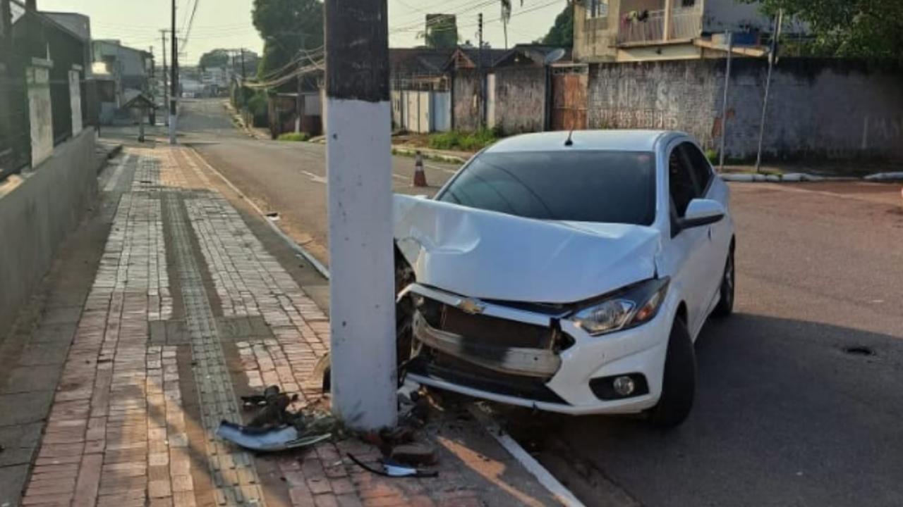 Carro branco danificado após colidir com poste em rua.