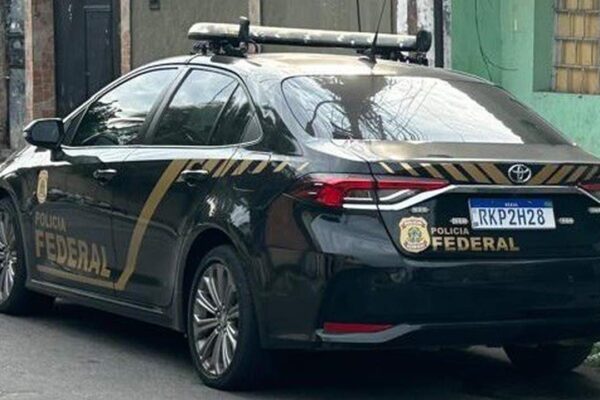 Carro da Polícia Federal estacionado em rua, com logotipos e sirene no teto.