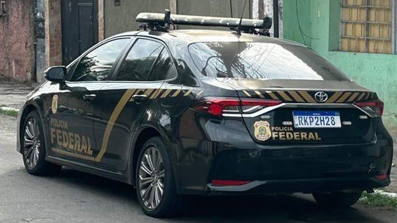 Carro da Polícia Federal estacionado em rua, com logotipos e sirene no teto.
