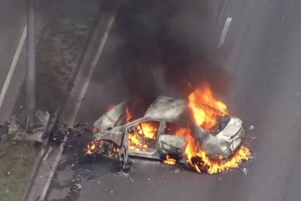 Carro em chamas na Avenida Brasil, com fumaça densa.