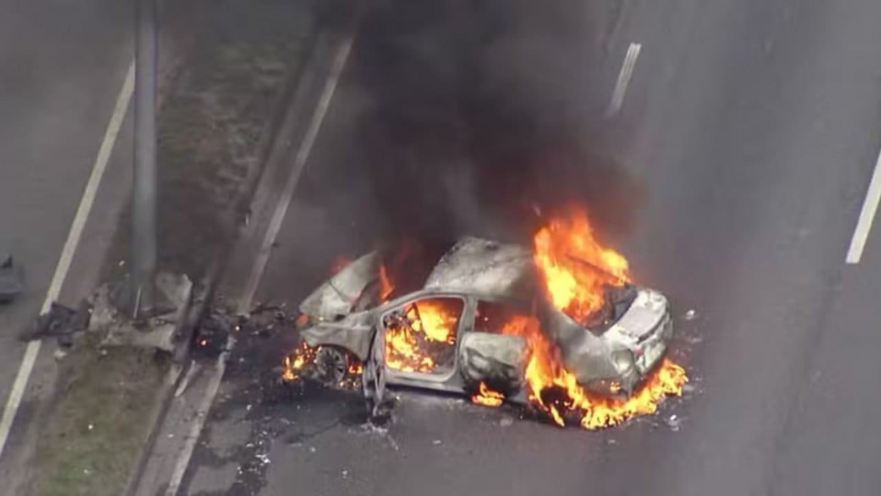 Carro em chamas na Avenida Brasil, com fumaça densa.
