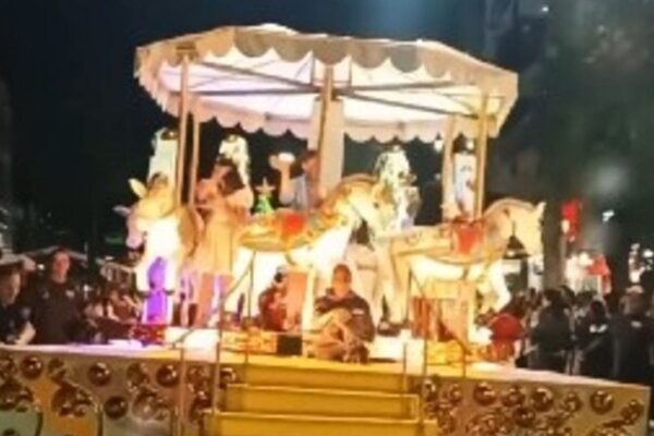 Carros alegóricos de Natal em Nova Friburgo, com detalhes em dourado e figuras de cavalos iluminados, e pessoas ao fundo.