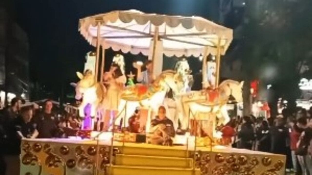 Carros alegóricos de Natal em Nova Friburgo, com detalhes em dourado e figuras de cavalos iluminados, e pessoas ao fundo.