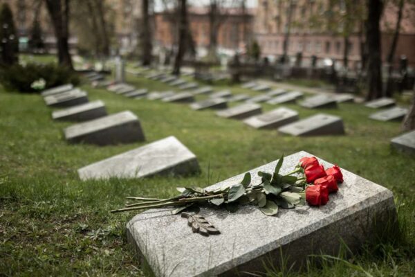 Cemitério com lápides e flores vermelhas em primeiro plano, em um dia nublado.