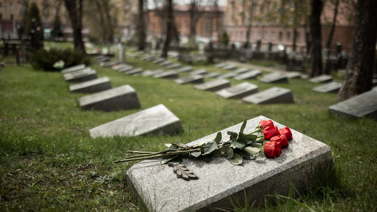 Cemitério com lápides e flores vermelhas em primeiro plano, em um dia nublado.