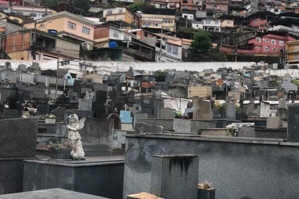 Cemitério São João Batista com casas no morro ao fundo