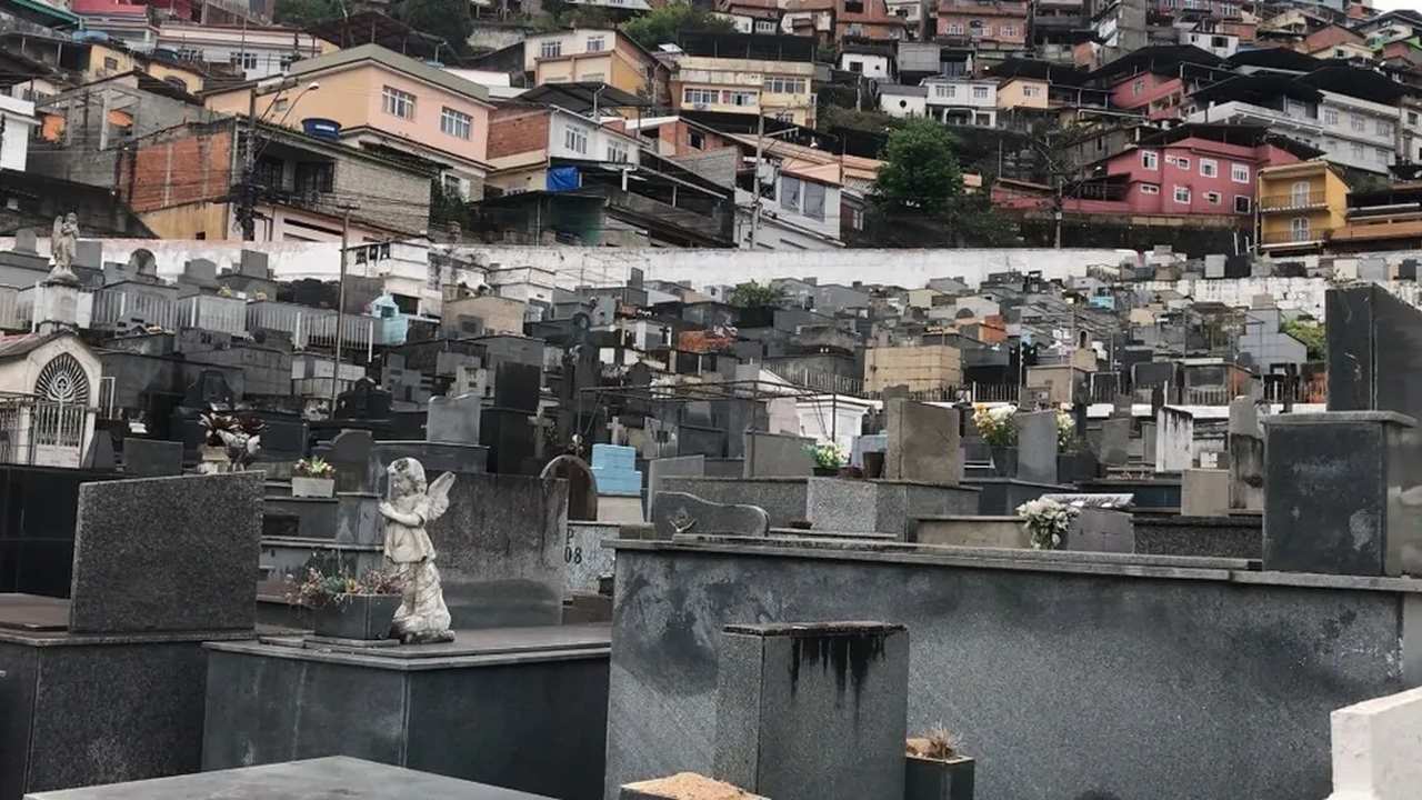 Cemitério São João Batista com casas no morro ao fundo