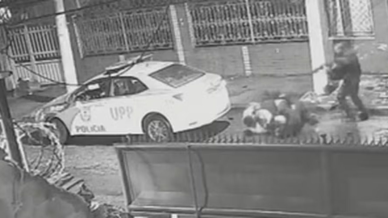 Cena de abordagem policial com carro da UPP e pessoas no chão.