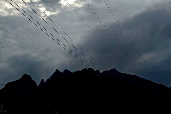 Céu nublado com silhueta de montanhas e cabos de energia, sob efeito da frente fria.