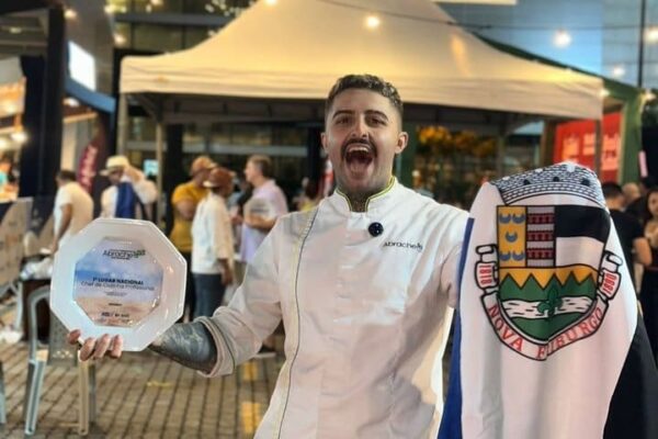 Chef João Vieira, de Nova Friburgo, sorri segurando um prêmio e uma bandeira, comemorando o título de Melhor Chef do Brasil em 2025.