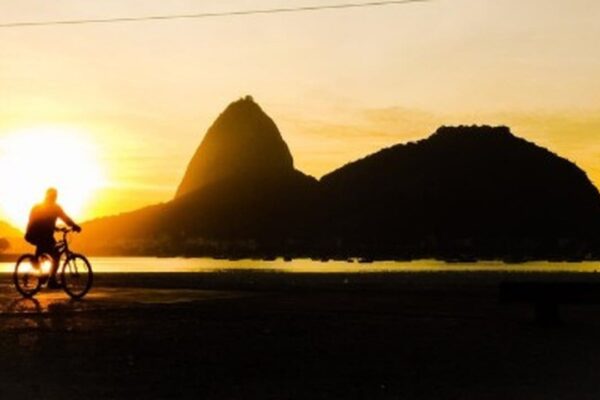 Ciclista na praia em frente ao Pão de Açúcar no Rio de Janeiro ao pôr do sol.
