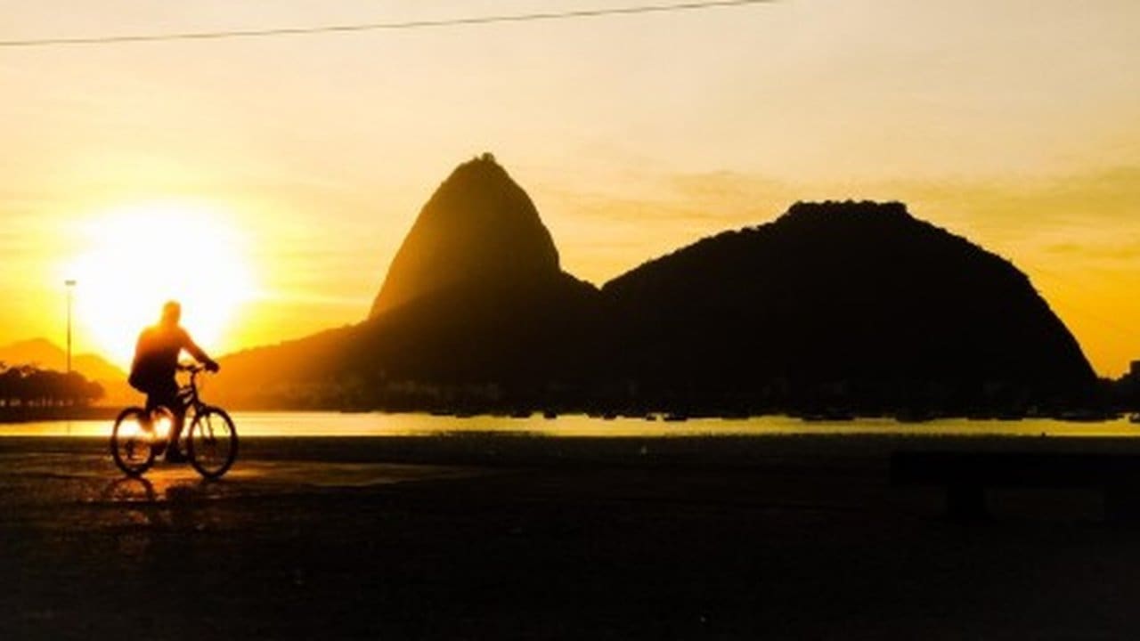 Ciclista na praia em frente ao Pão de Açúcar no Rio de Janeiro ao pôr do sol.