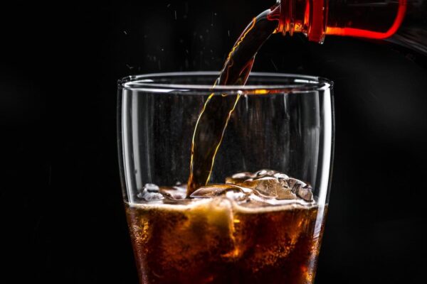 Coca-cola sendo servida em um copo com gelo, com fundo preto