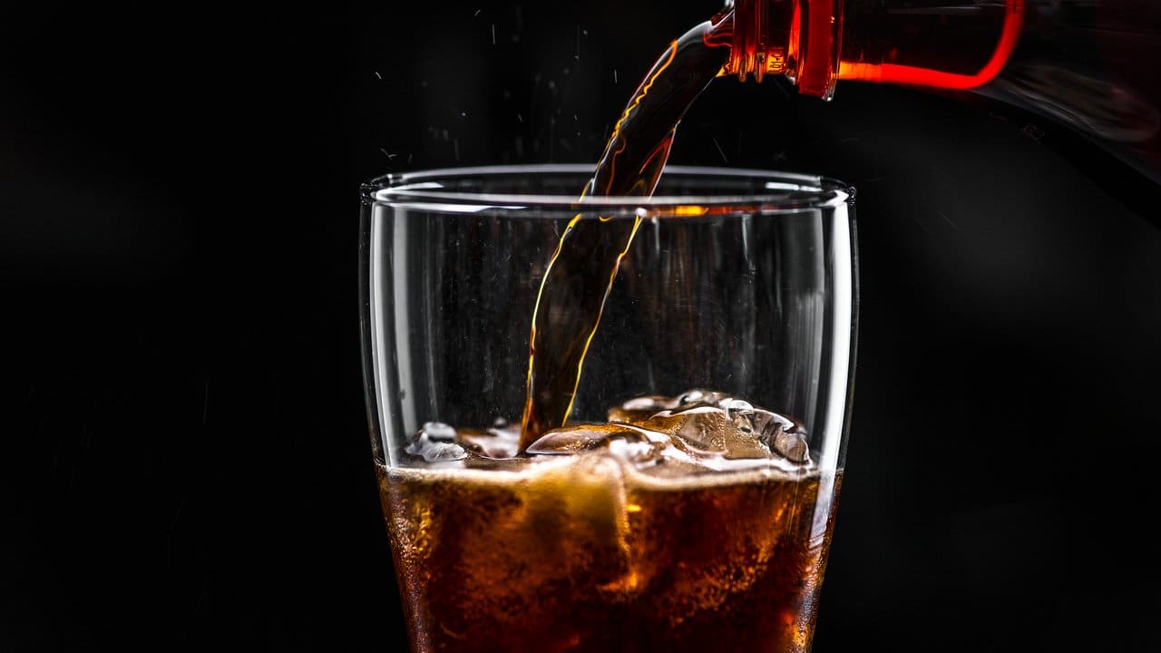 Coca-cola sendo servida em um copo com gelo, com fundo preto