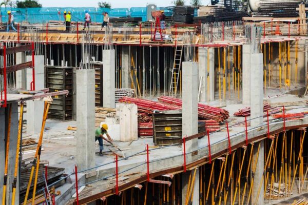 Construção em andamento em Nova Friburgo, com trabalhadores e estruturas de concreto e madeira.